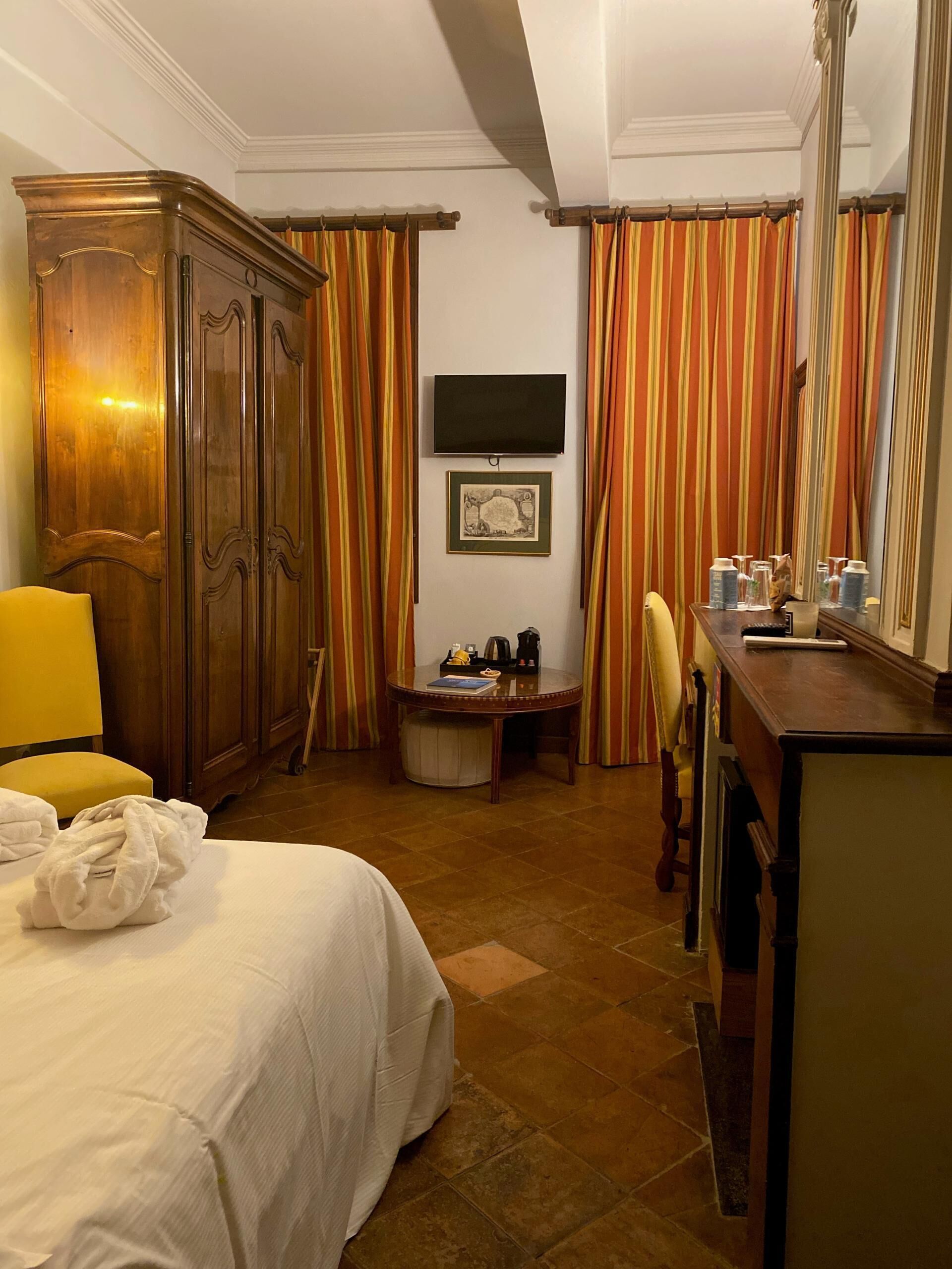 Una habitación de hotel con cama, escritorio, silla, televisor y armario.