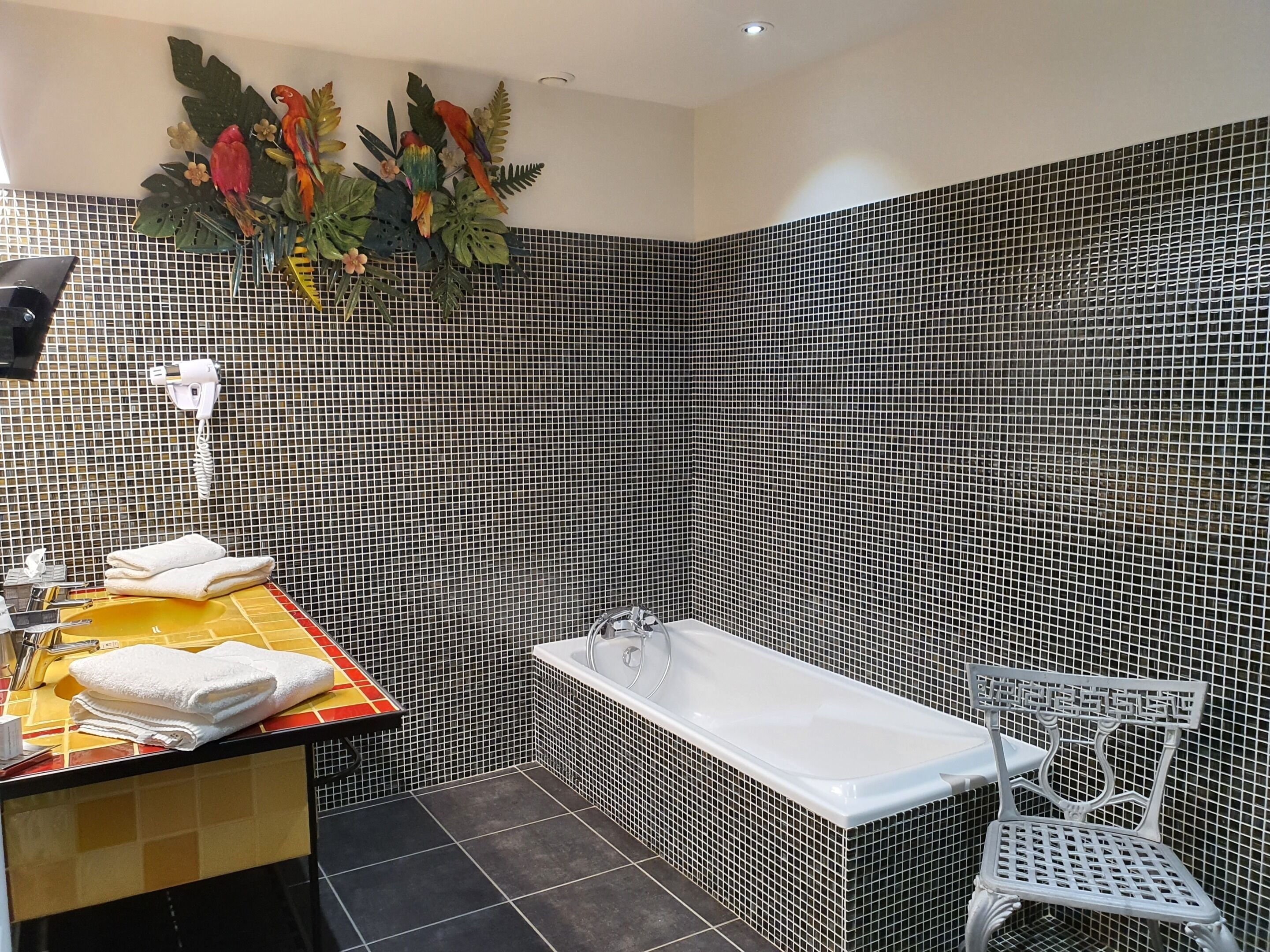 Un baño con pared de azulejos blanco y negro, una bañera blanca, una silla blanca y un lavabo con encimera amarilla.