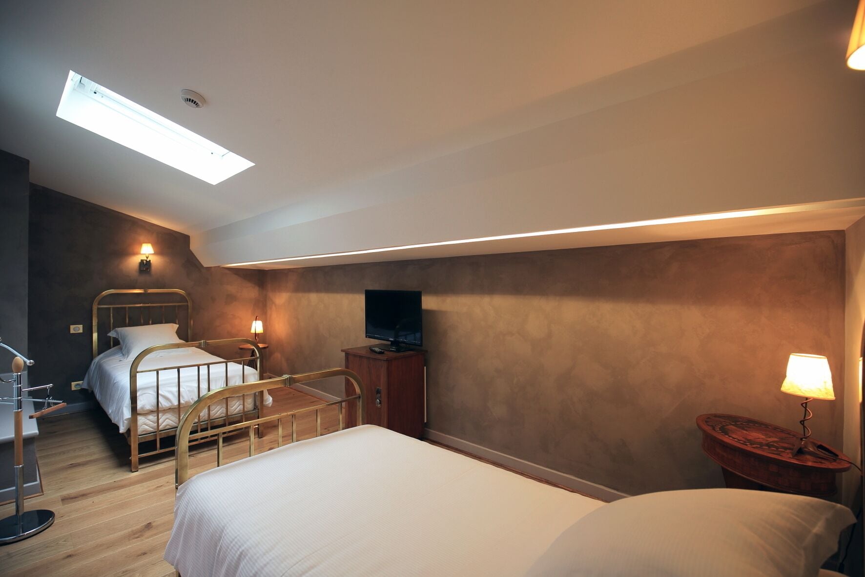 Habitación de hotel con dos camas, un escritorio, un televisor y un tragaluz.