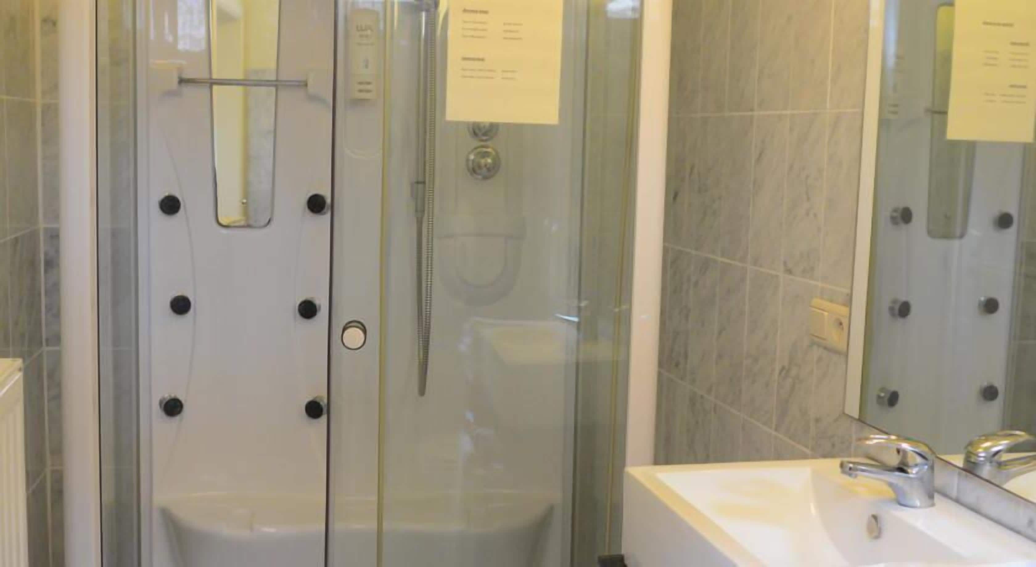 A glass-enclosed shower stall with a control panel and a hand shower.