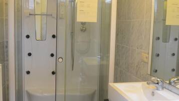 A glass-enclosed shower stall with a control panel and a hand shower.