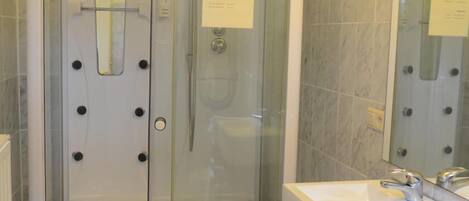 A glass-enclosed shower stall with a control panel and a hand shower.