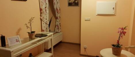 A room with a white console table, a small round table, a radiator, and a wall-mounted light switch.