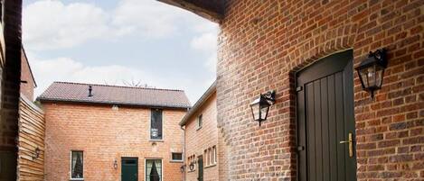 Un patio con un edificio de ladrillo, un área de estar techada y una puerta con un farol.
