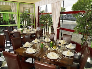 A restaurant with a checkered floor, wooden tables set with white tablecloths, and brown leather chairs.