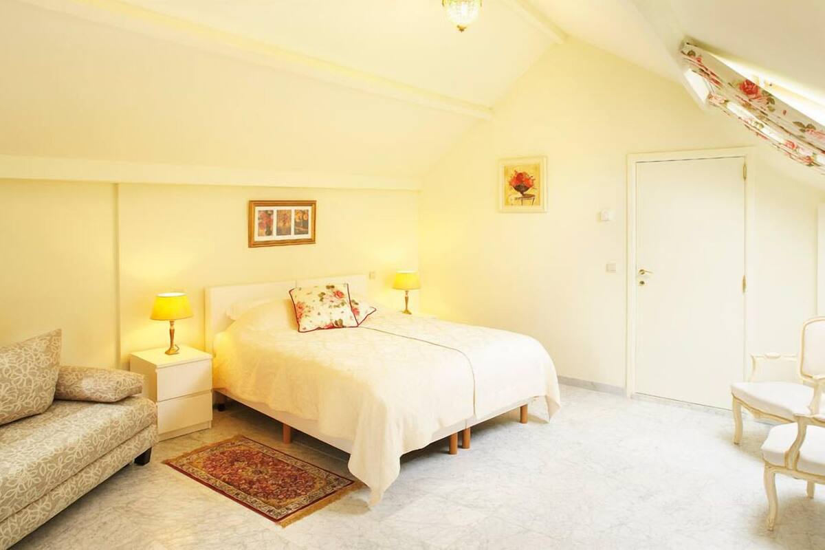 Een slaapkamer met een bed, een nachtkastje, een lamp, een stoel en een deur.
