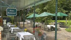 Een buitenterras met tafels en stoelen, een bord met daarop 'Texas Restaurant' en groene parasols voor beschutting.