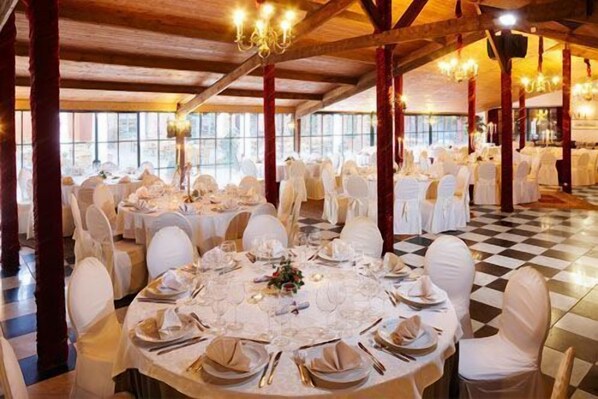 Un salón de banquetes con mesas redondas dispuestas para un evento formal, con candelabros y un suelo a cuadros.