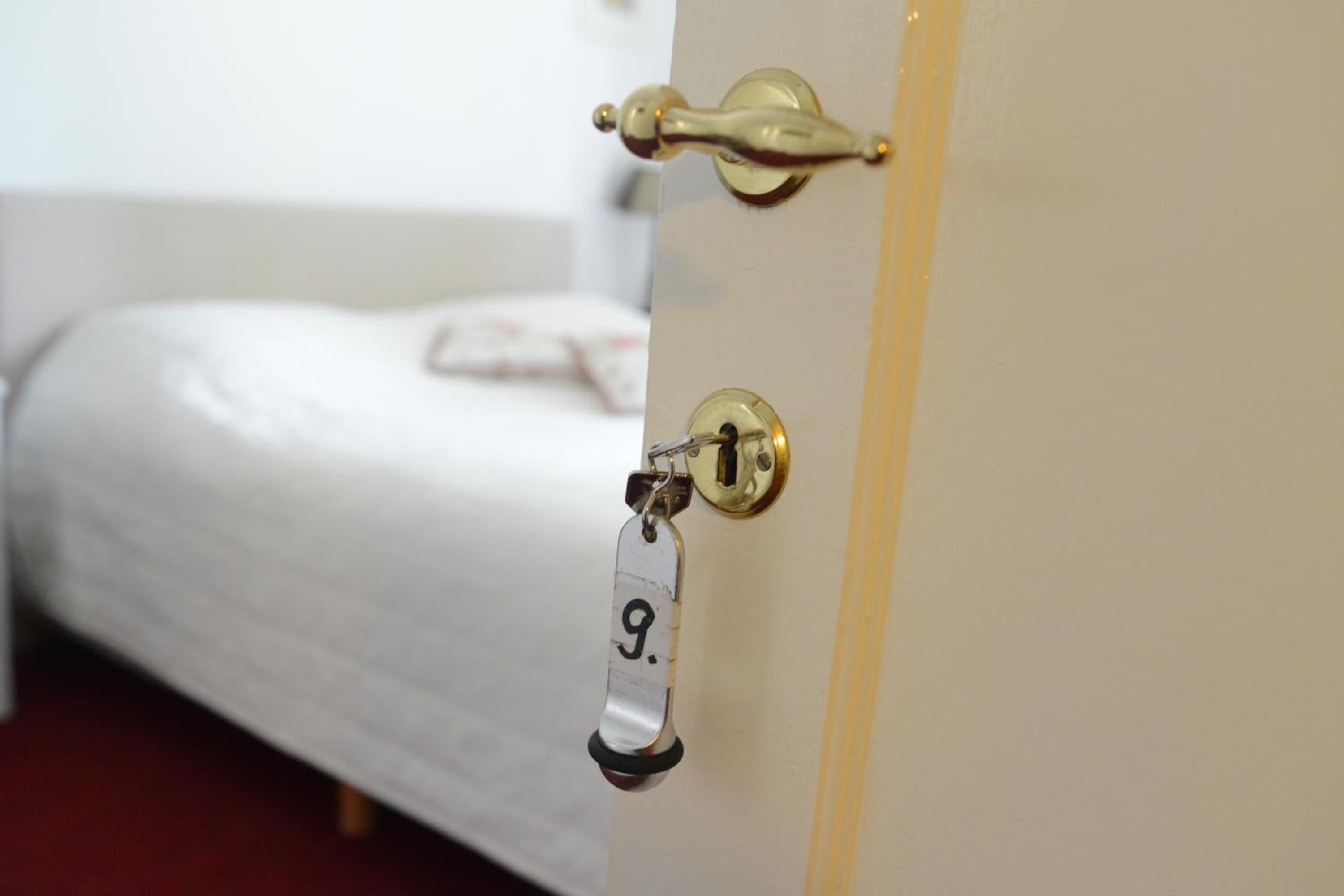 A door with a brass handle and a keyhole, a bed with white bedding, and a tag with the number 9.