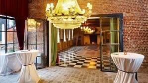 Een kamer met een geruite vloer, een kroonluchter en twee ronde tafels met witte tafellakens.