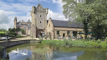 Un edificio histórico con una torre, un patio con asientos al aire libre y un estanque con cisnes.