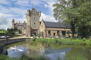 A historic building with a tower, a courtyard with outdoor seating, and a pond with swans.