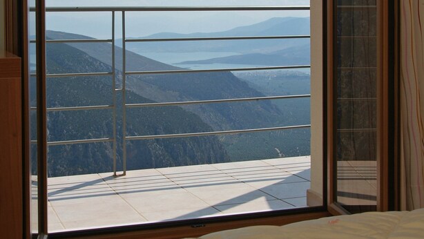 A bedroom with a large window offering a view of mountains and a lake. - Tholos (Delphi)