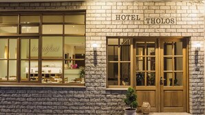 A hotel with a stone facade, large windows, and a sign reading "HOTEL THOLOS". - Tholos (Delphi)