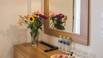 A bathroom vanity with a mirror, a television mounted above, and a vase with flowers.