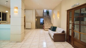 A spacious lobby with a marble floor, a staircase, a reception desk, and a seating area with a sofa and cushions. - Tholos (Delphi)