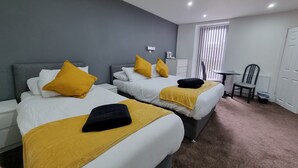 Ein Hotelzimmer mit zwei Betten, jeweils mit weißer Bettwäsche und gelben Kissen, einem kleinen Tisch, einem Stuhl und einem Heizkörper.