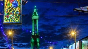 Ein nächtlicher Blick auf einen hohen Turm mit grüner Beleuchtung, umgeben von Lichterketten und einem Buntglasfenster.