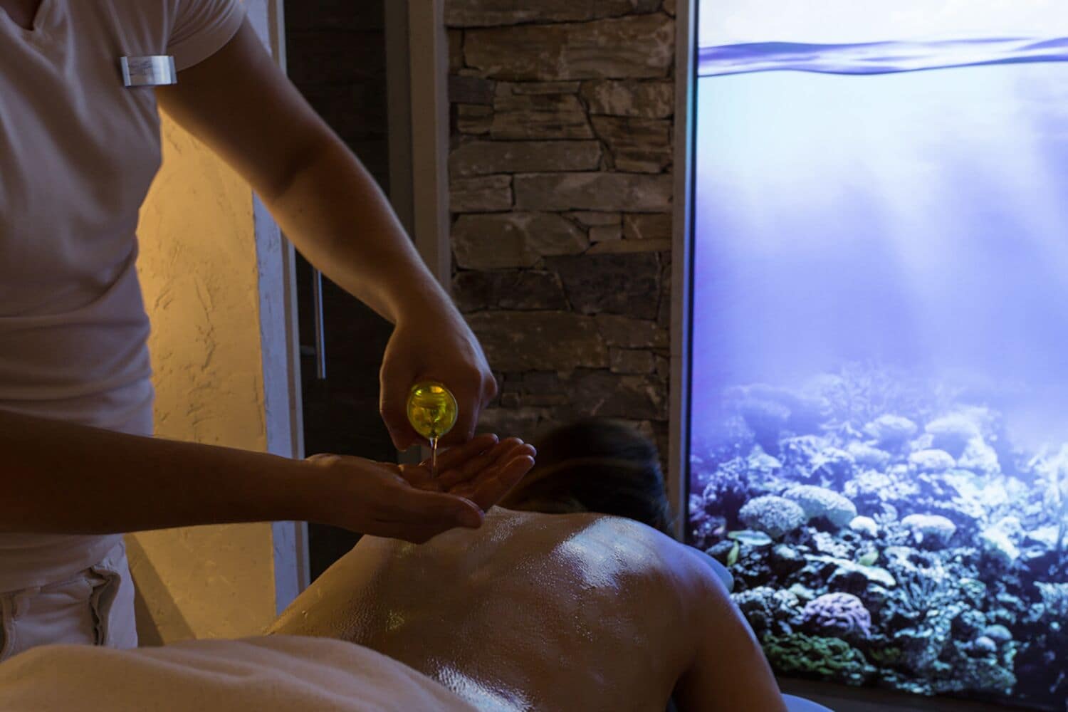 Eine Person erhält eine Massage, im Hintergrund eine Steinsäule und ein Aquarium.