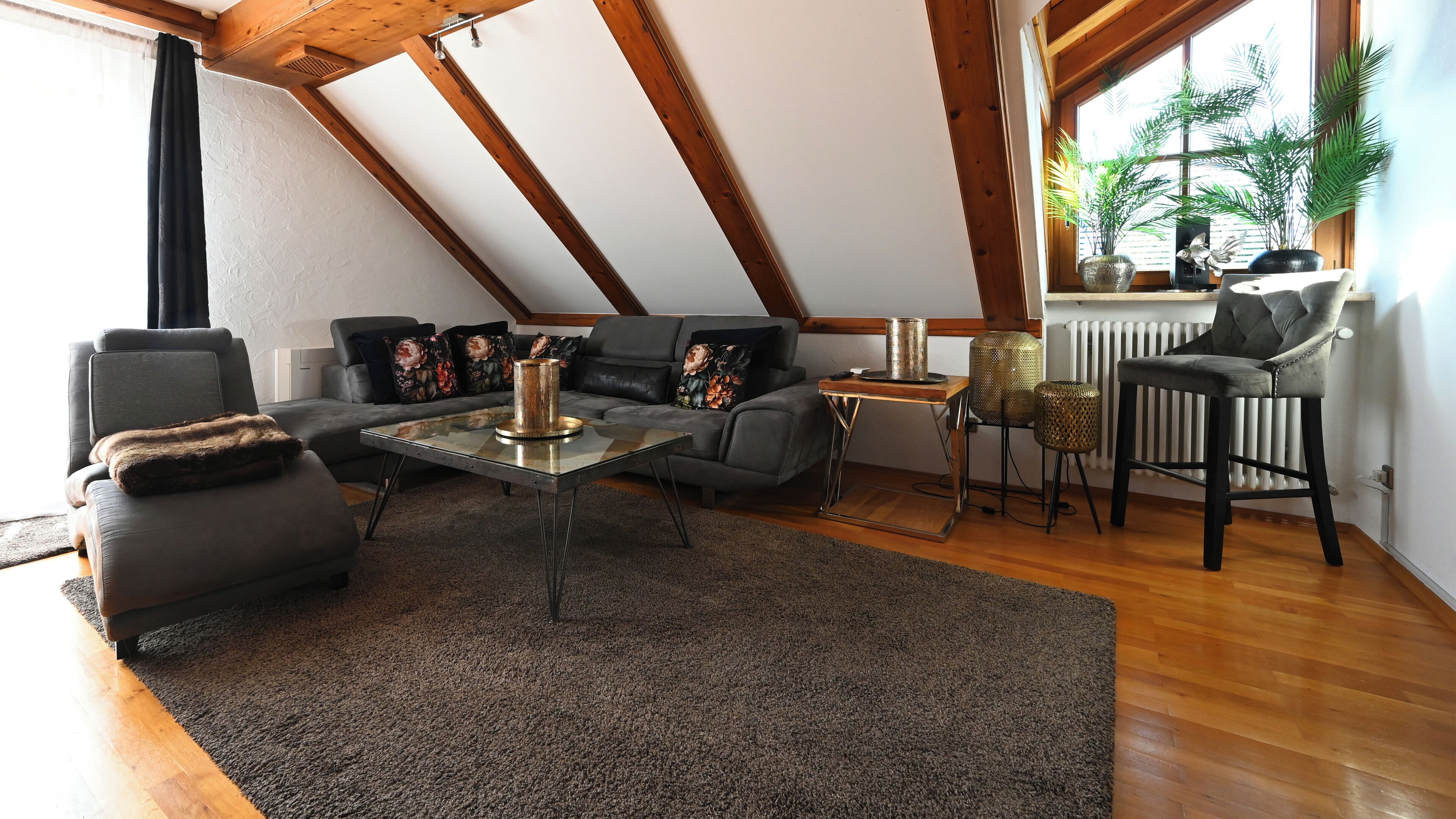 A modern living room with a sloped ceiling, a sectional sofa, a glass coffee table, and a radiator.