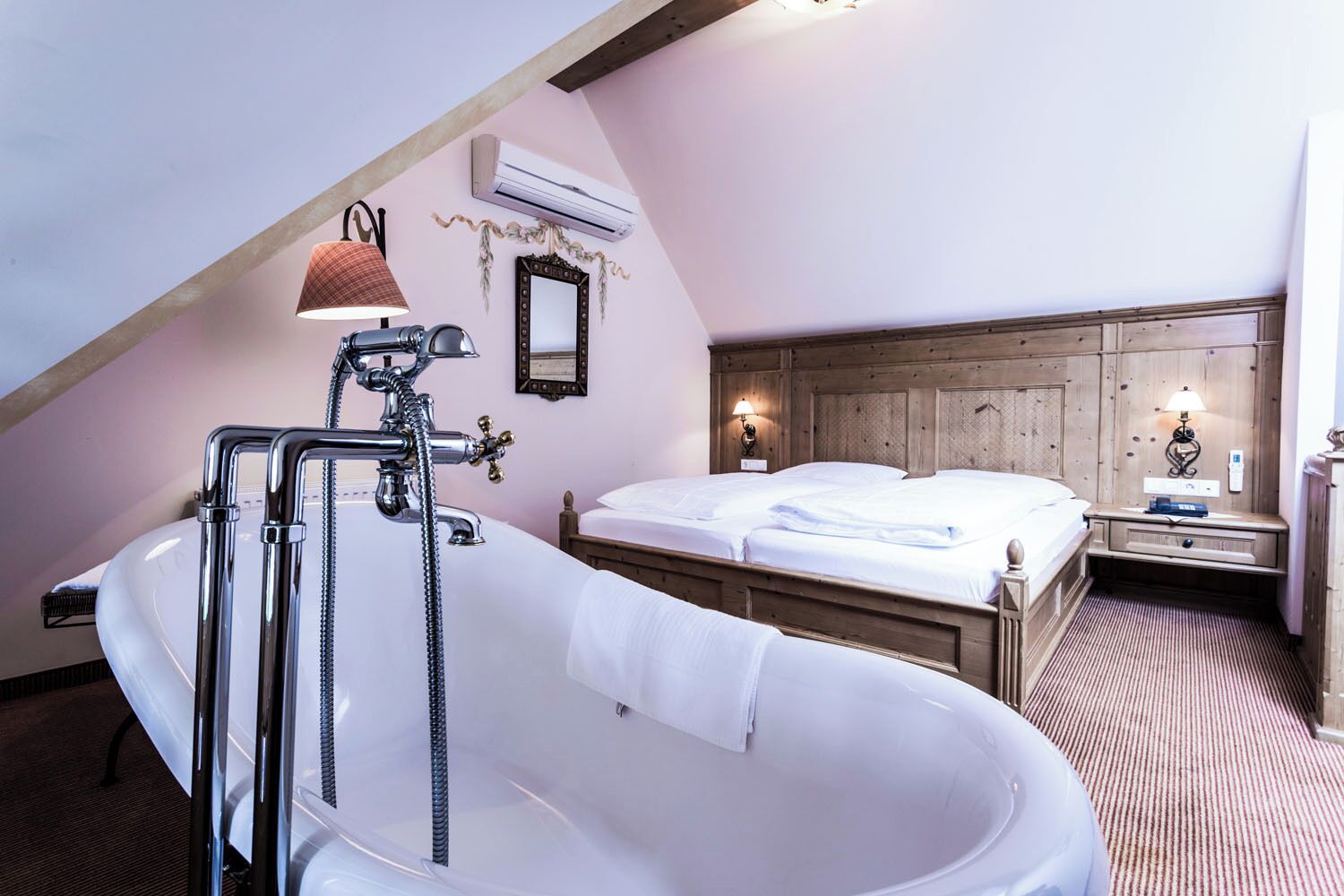Une chambre avec une grande baignoire, une tête de lit en bois et une table de chevet avec une lampe.