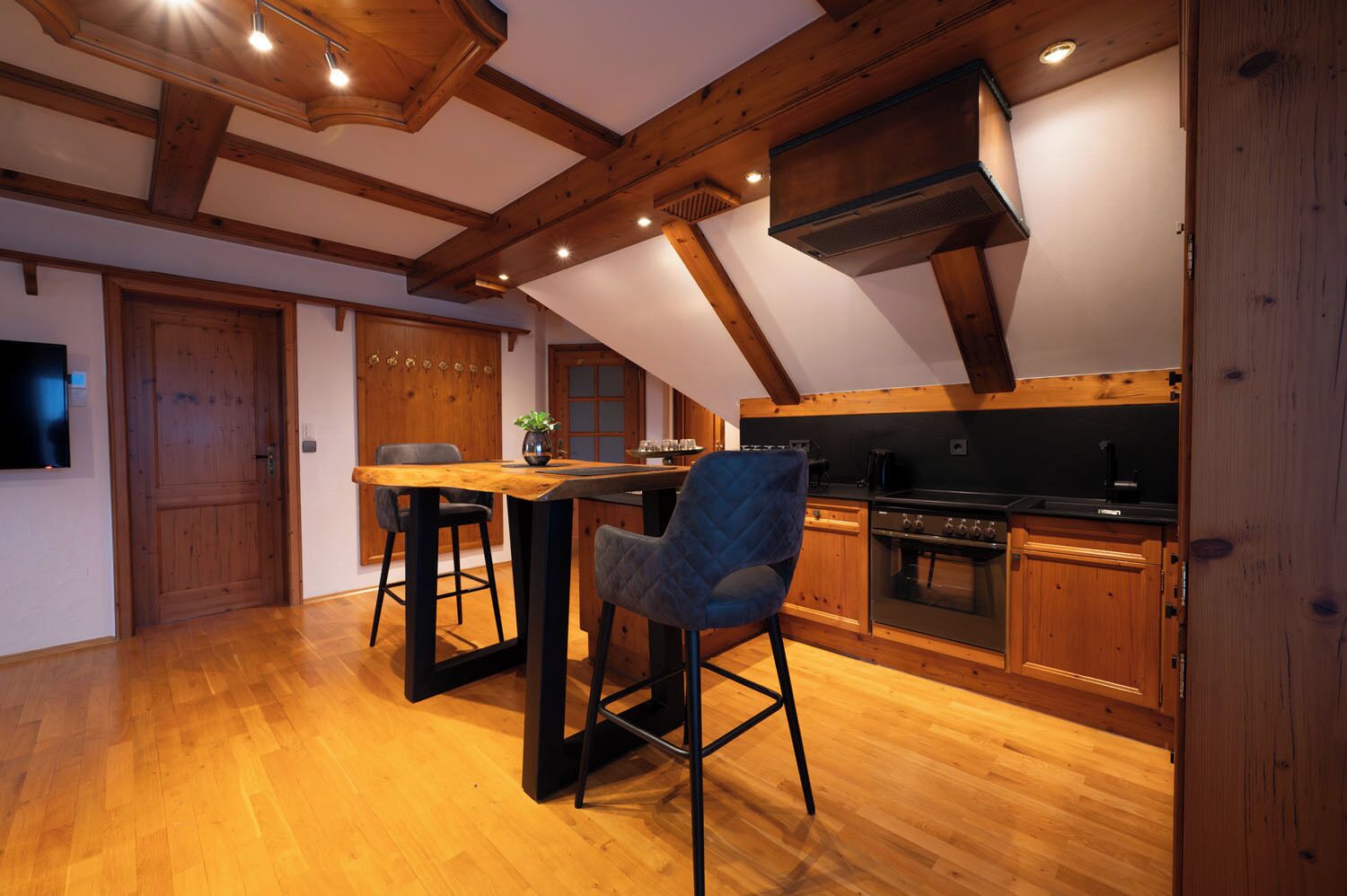 A kitchen with wooden beams, a dining table, two chairs, and a stove.