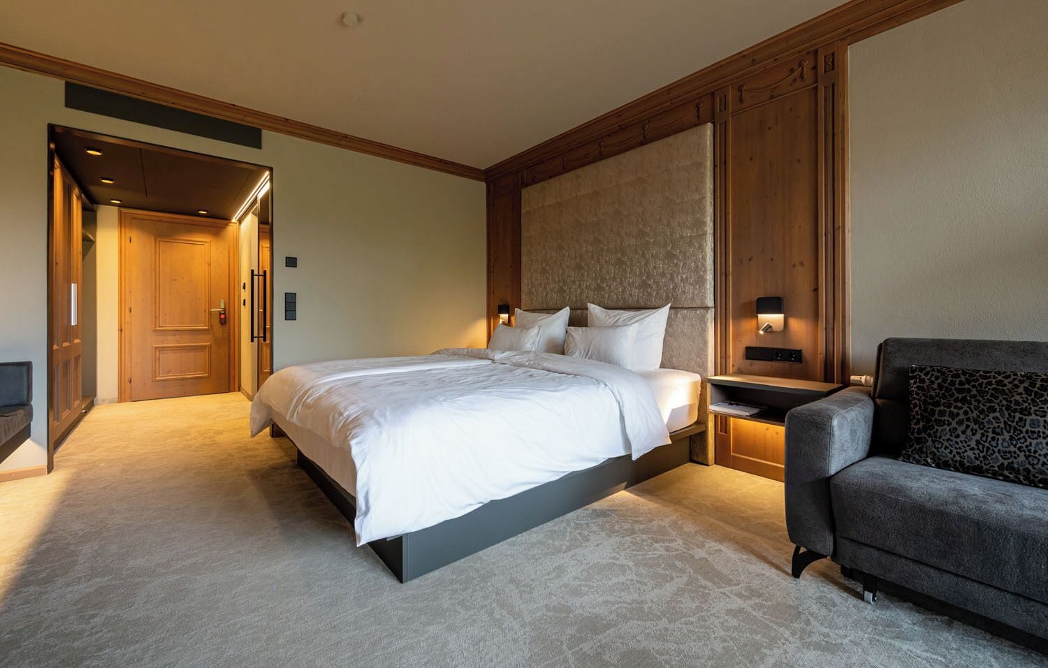 A hotel room with a large bed, a sofa, a nightstand, and a wooden headboard.
