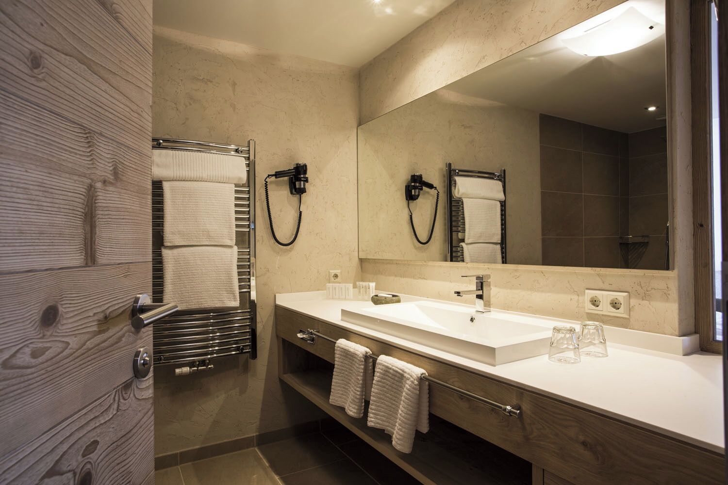 A modern bathroom with a wooden vanity, a large mirror, and a towel rack.
