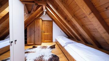 A bedroom with a sloped ceiling, wooden beams, a large wardrobe, a bed, and a cowhide rug.