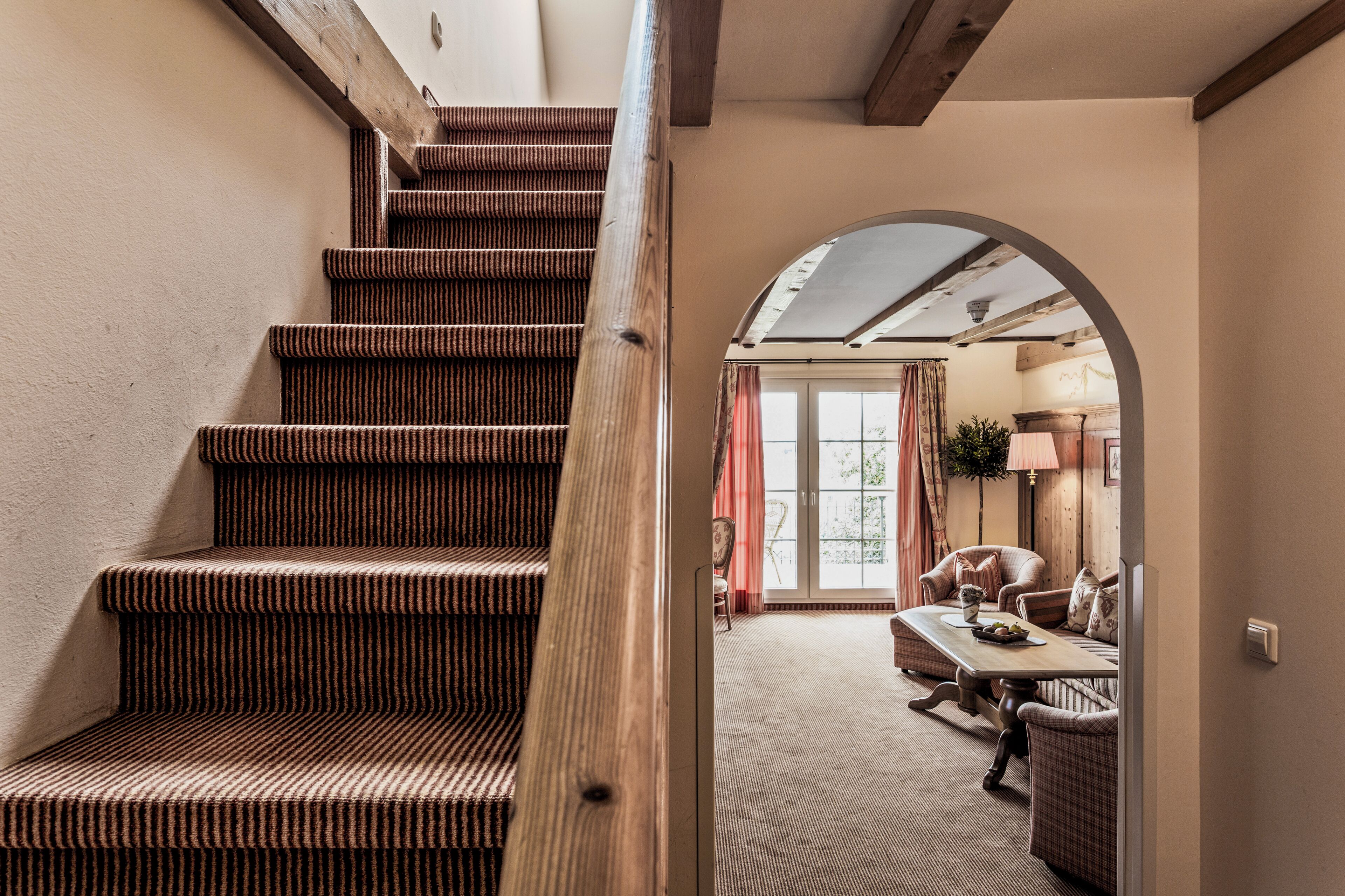 A staircase with striped carpet leading to a room with a dining area and a view of the outdoors.