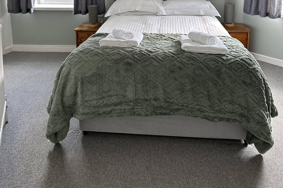 A bedroom with a bed, a window, curtains, a bedside table, and a hanging light fixture.