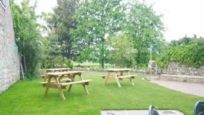En græsbelagt udendørs plads med picnicborde og en stenvæg.