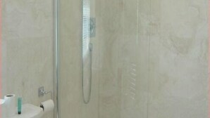 Et badeværelse med brusekabine i glas, en hvid vask og et toilet.