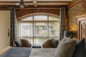 A cozy room with a bed, two armchairs, a table, and a fireplace. - The Barns at Thorpe Market (Norwich)