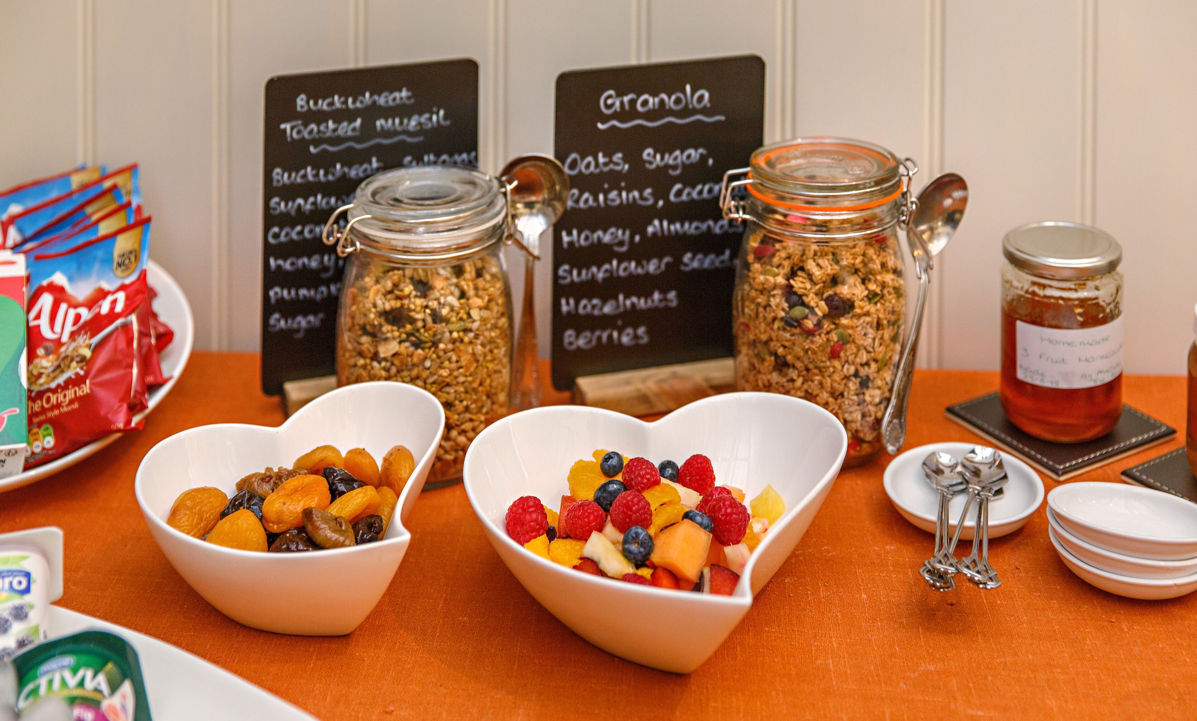 A breakfast buffet with bowls of granola and fruit, and jars of granola and jam.