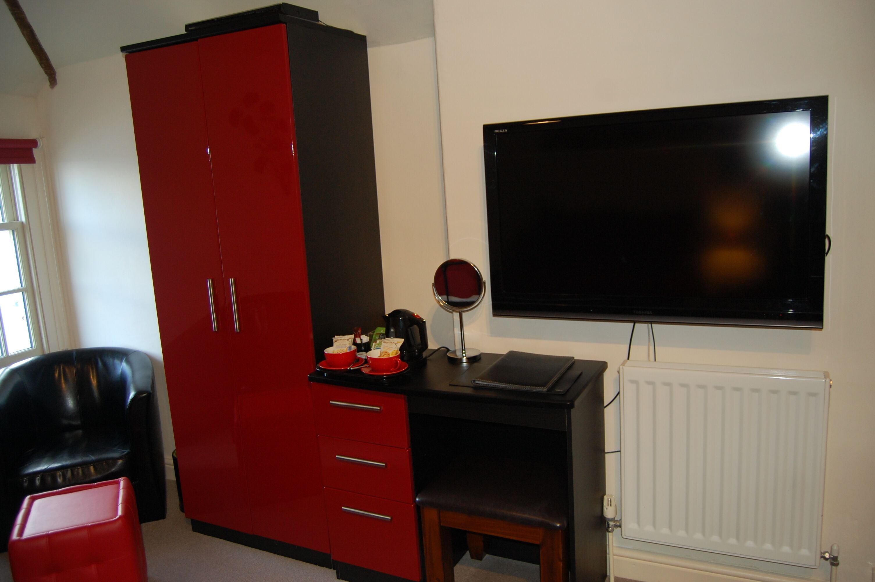 A room with a red wardrobe, a black desk with a mirror, a television, and a radiator.
