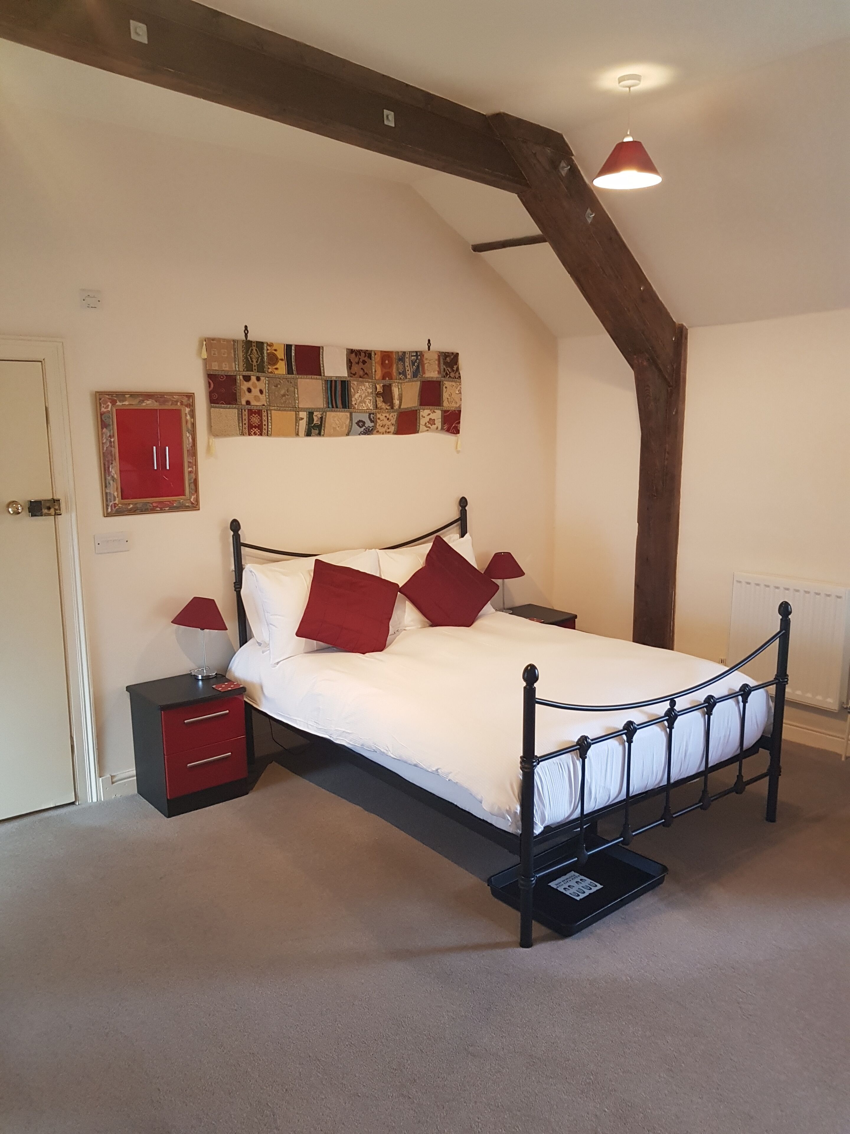 A bedroom with a bed, nightstands, a red cabinet, a quilt, and a wooden ceiling beam.