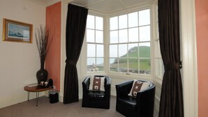 A room with two black leather chairs, a small table with a vase and a cup, and a window with curtains. - The Olive Branch (Ilfracombe)