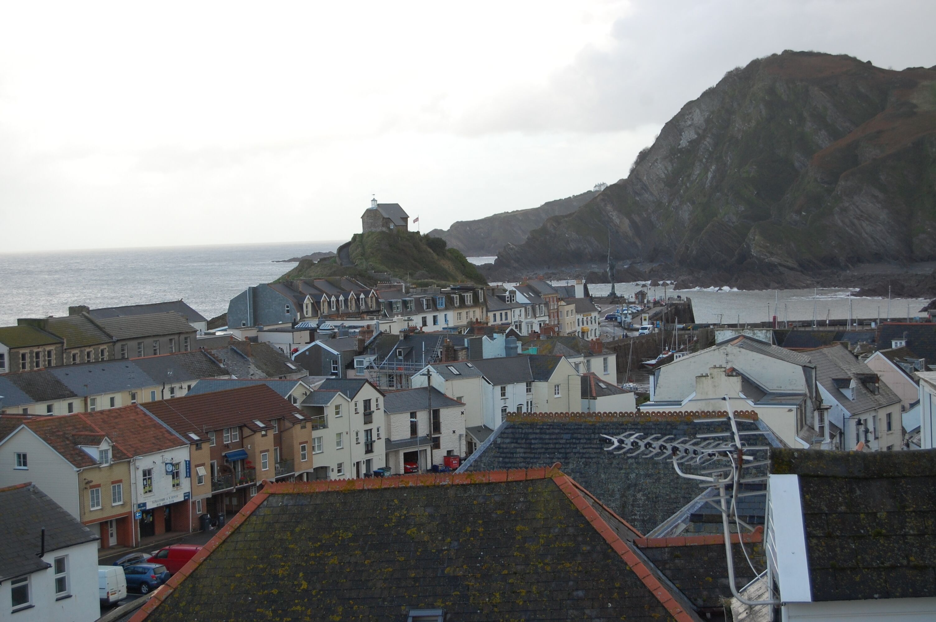 A coastal town with historic buildings, a prominent hilltop structure, and a view of the sea.