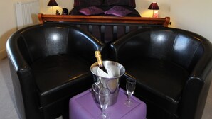 A room with a black leather sofa, a purple ottoman, a bedside table with a lamp, and a bed with purple bedding. - The Olive Branch (Ilfracombe)