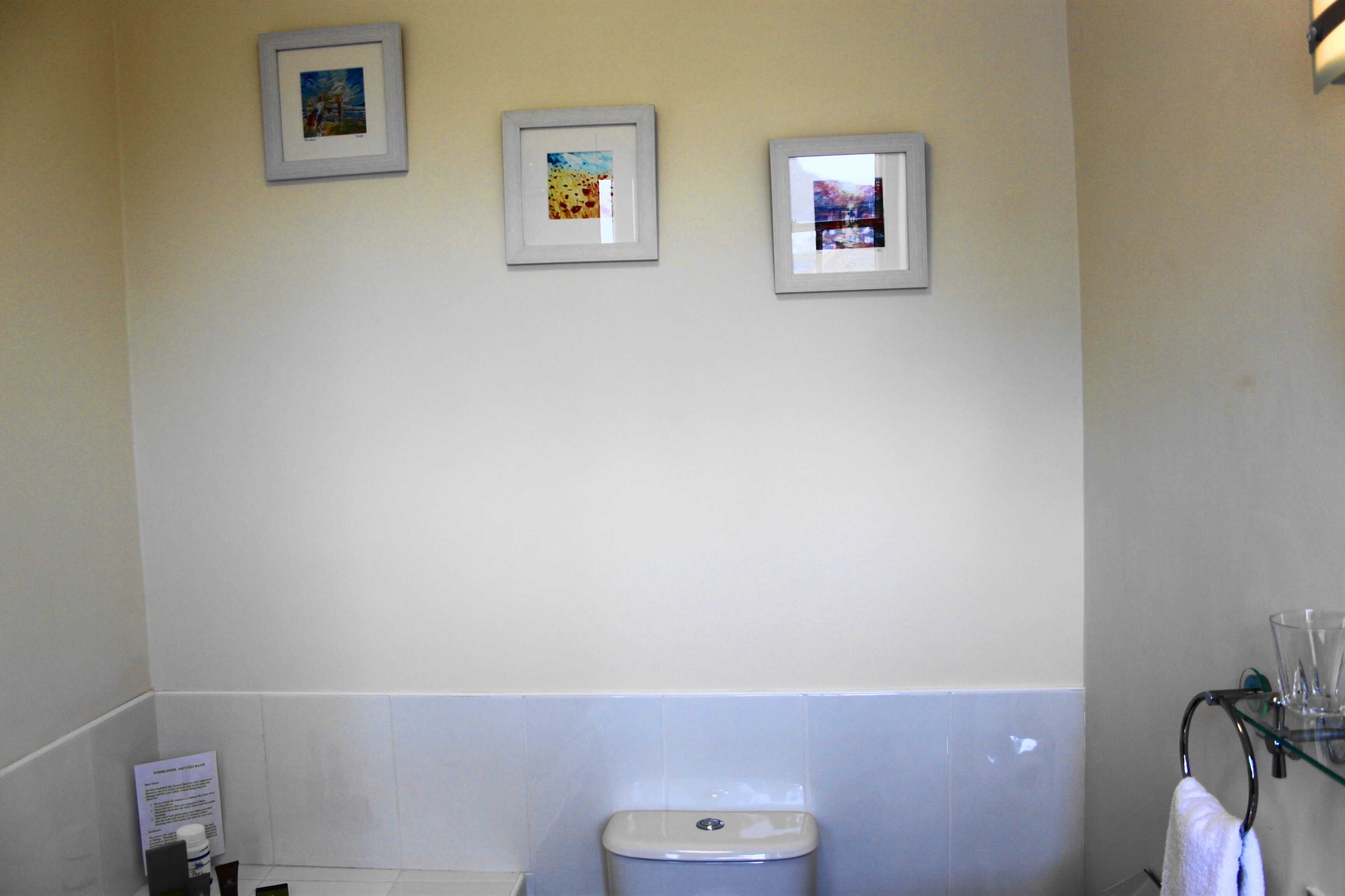 Un baño con un inodoro, un estante de vidrio con una toalla y tres cuadros en la pared.