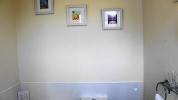 Un baño con un inodoro, un estante de vidrio con una toalla y tres cuadros en la pared.