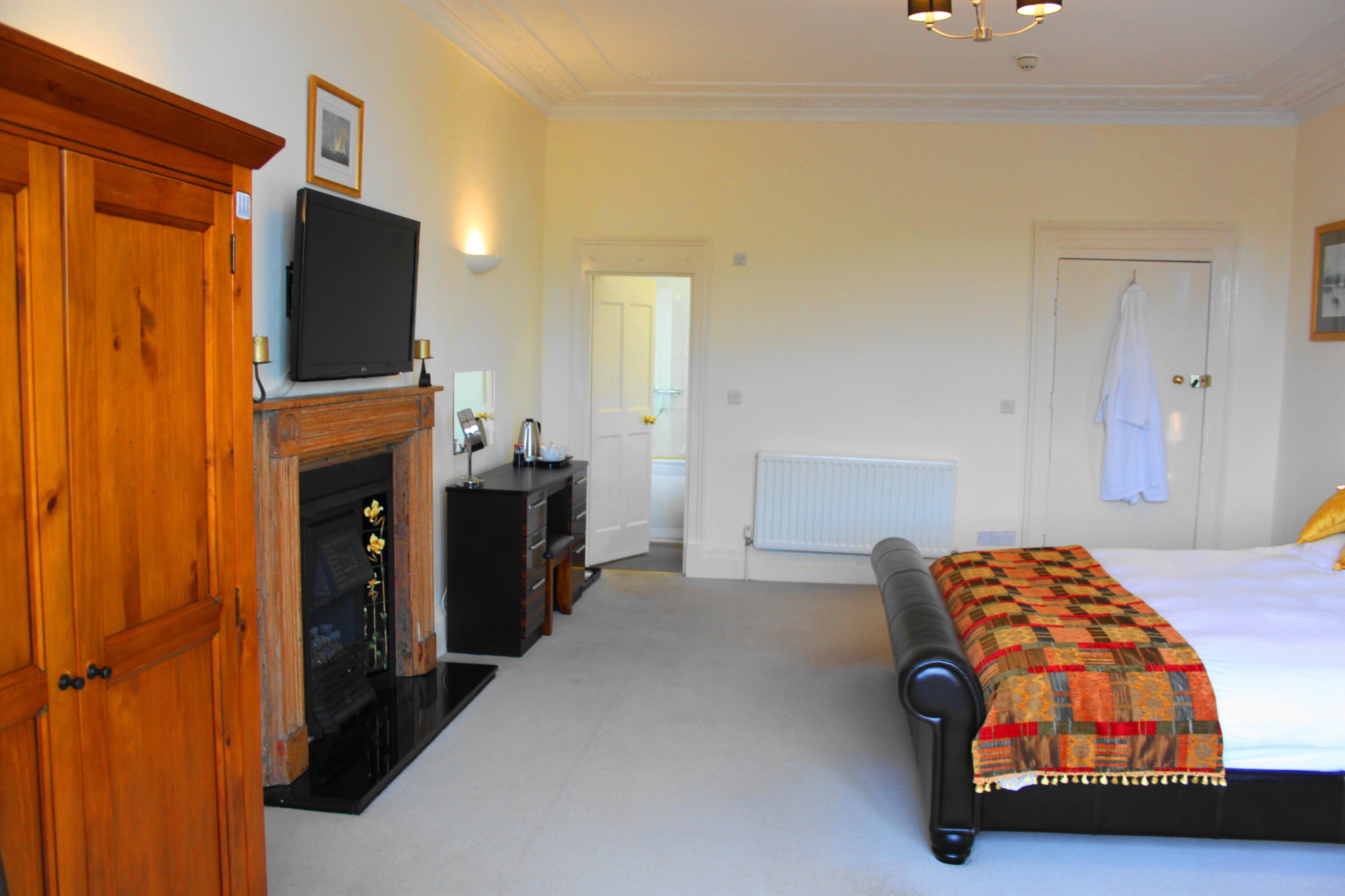 A bedroom with a bed, a wooden wardrobe, a television, a fireplace, and a door leading to another room.