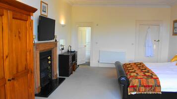 A bedroom with a bed, a wooden wardrobe, a television, a fireplace, and a door leading to another room.