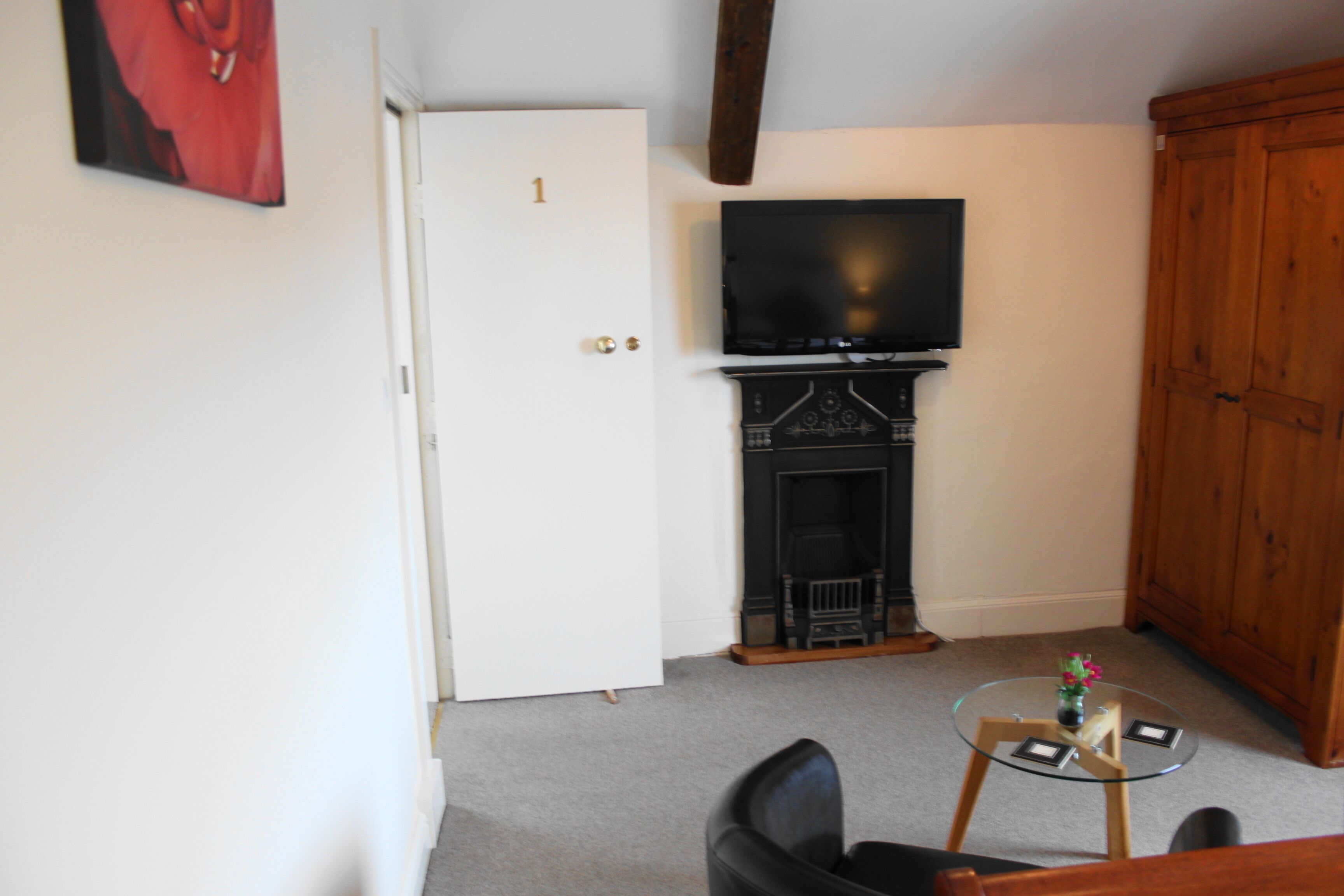 Ein Zimmer mit einer weißen Tür, die die Nummer 1 trägt, einem Kamin, einem darüber montierten Fernseher und einem kleinen runden Tisch mit einer Vase.