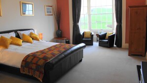 A spacious bedroom with a large bed, two armchairs, a wooden wardrobe, and a window with curtains. - The Olive Branch (Ilfracombe)