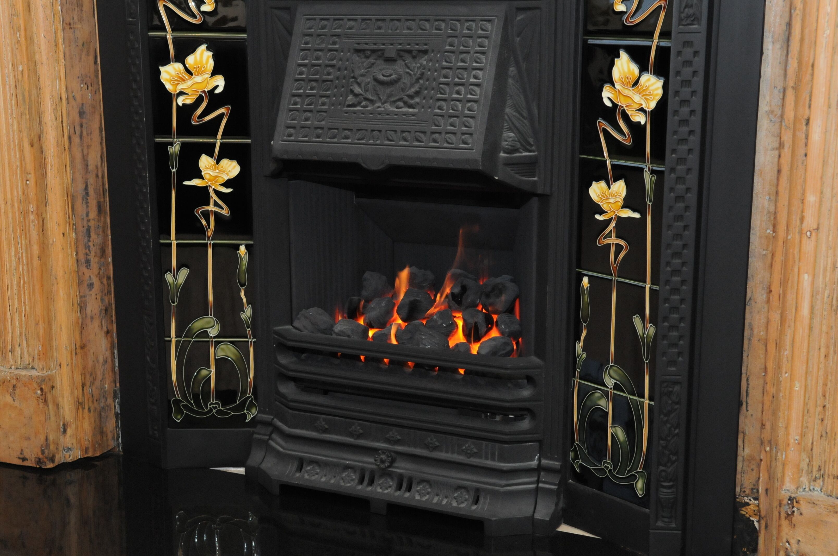 Una estufa de leña negra con detalles de metal decorativo y fuego encendido en su interior.