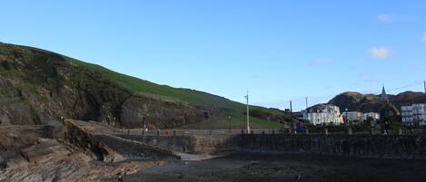 Eine Küstenlandschaft mit einem felsigen Strand, einer kleinen Brücke und Gebäuden im Hintergrund.