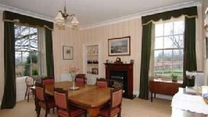 Une salle à manger avec une table et des chaises en bois, une cheminée et une vue sur l’extérieur.