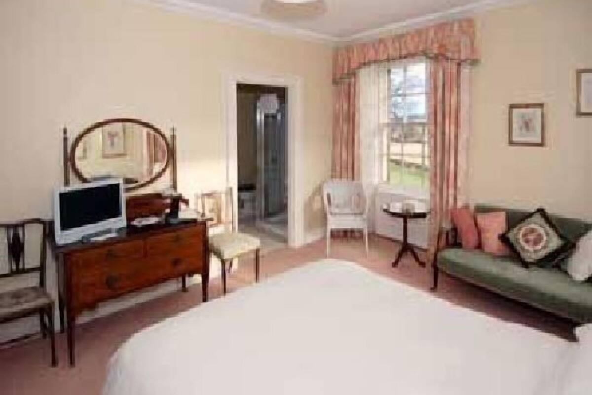 A bedroom with a bed, a dresser, a chair, a small table, and a television.